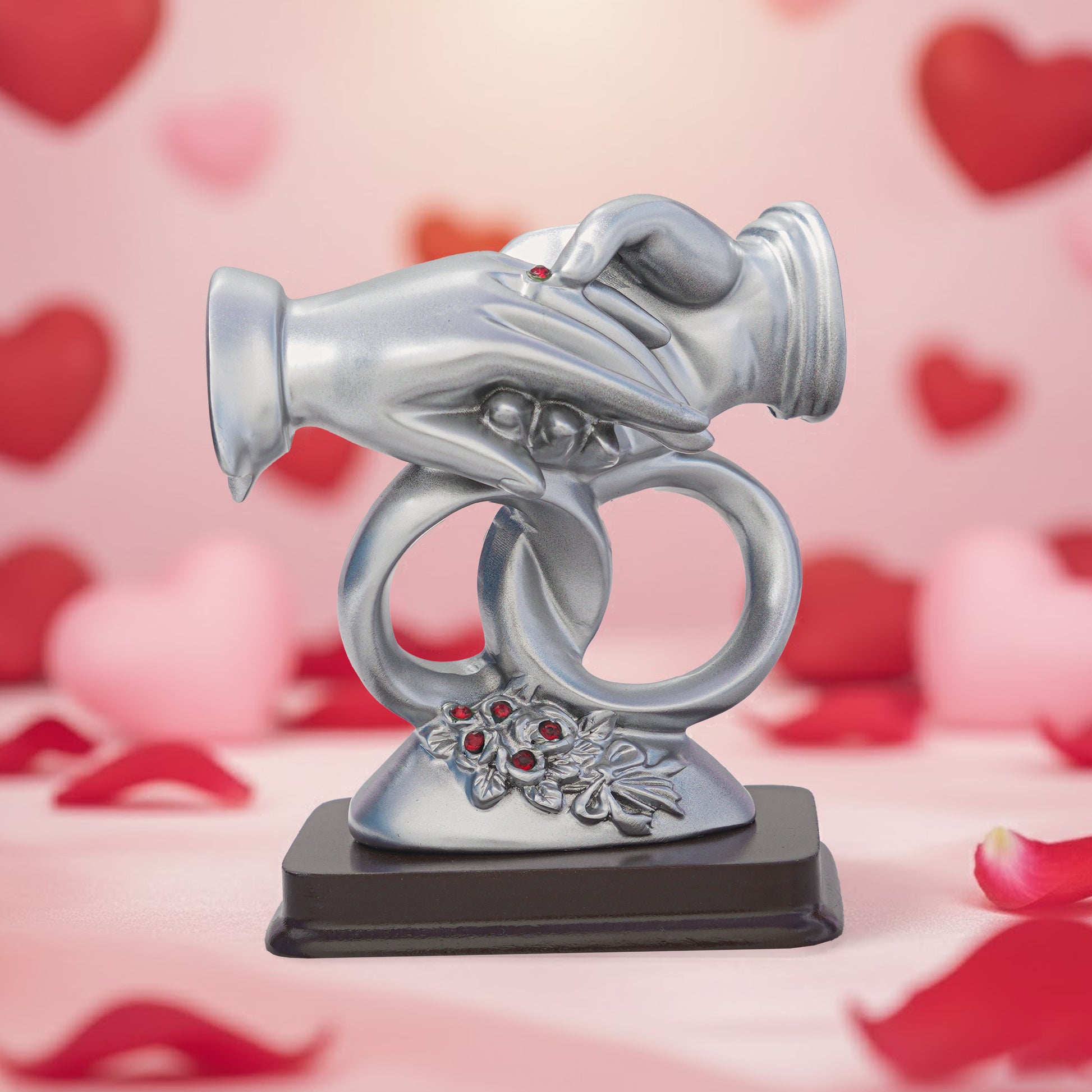 Decorative silver ring holder with red gemstones on a pink background with heart shapes